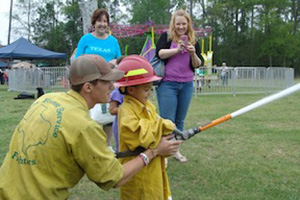 A firefighter helping a child shoot a small fire hose