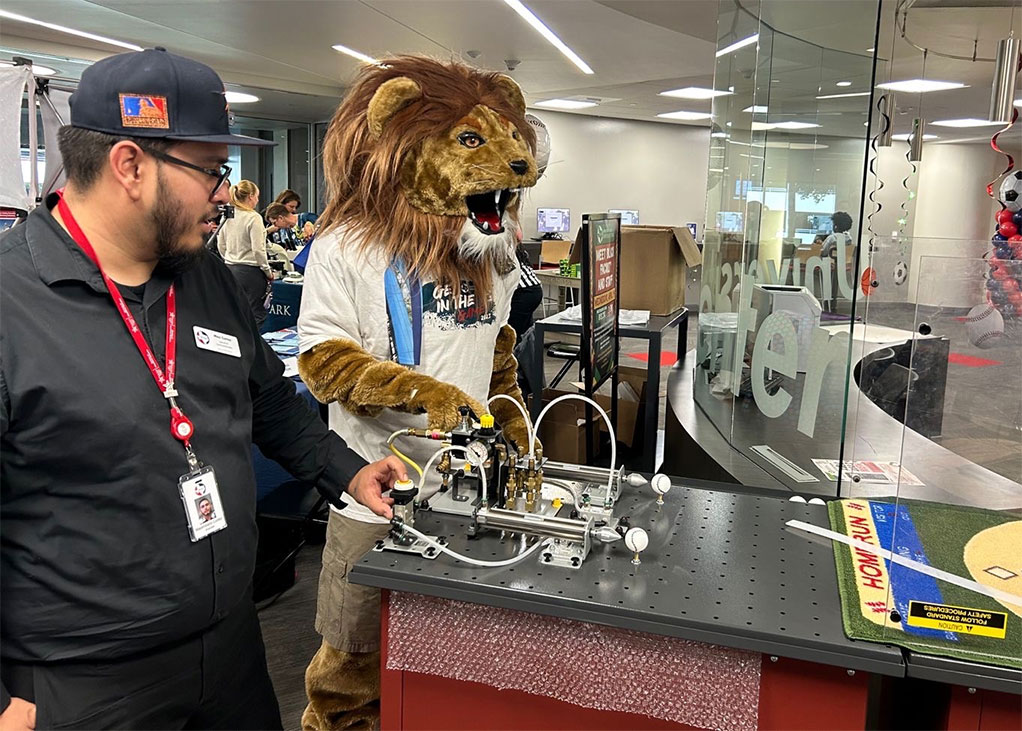 Lone Star College-University Park mascot Leo and Career and Education (CE) Specialist Maximiliano  Cortez review the parts of a hydraulic trainer during a recent campus event.