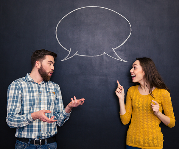 Man and woman standing in front of a chalkboard with a speech bubble drawn on it.