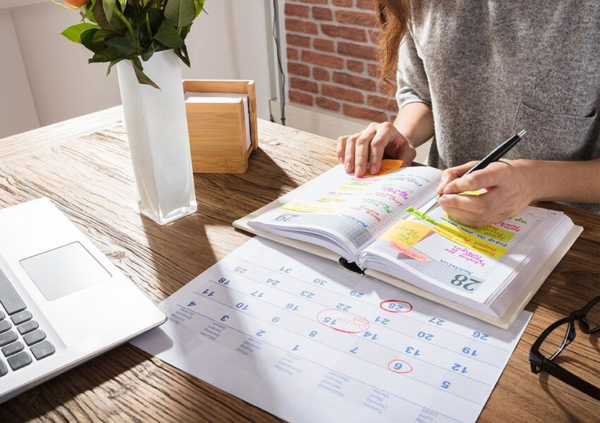 woman planning her schedule with book, calendar and laptop