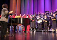 Dr. Lis Morales conducts a large group of music students arranged on risers onstage for a music concert.