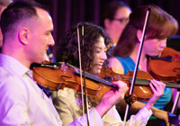 Violinists prepare for a song onstage in the Performing Arts Center.