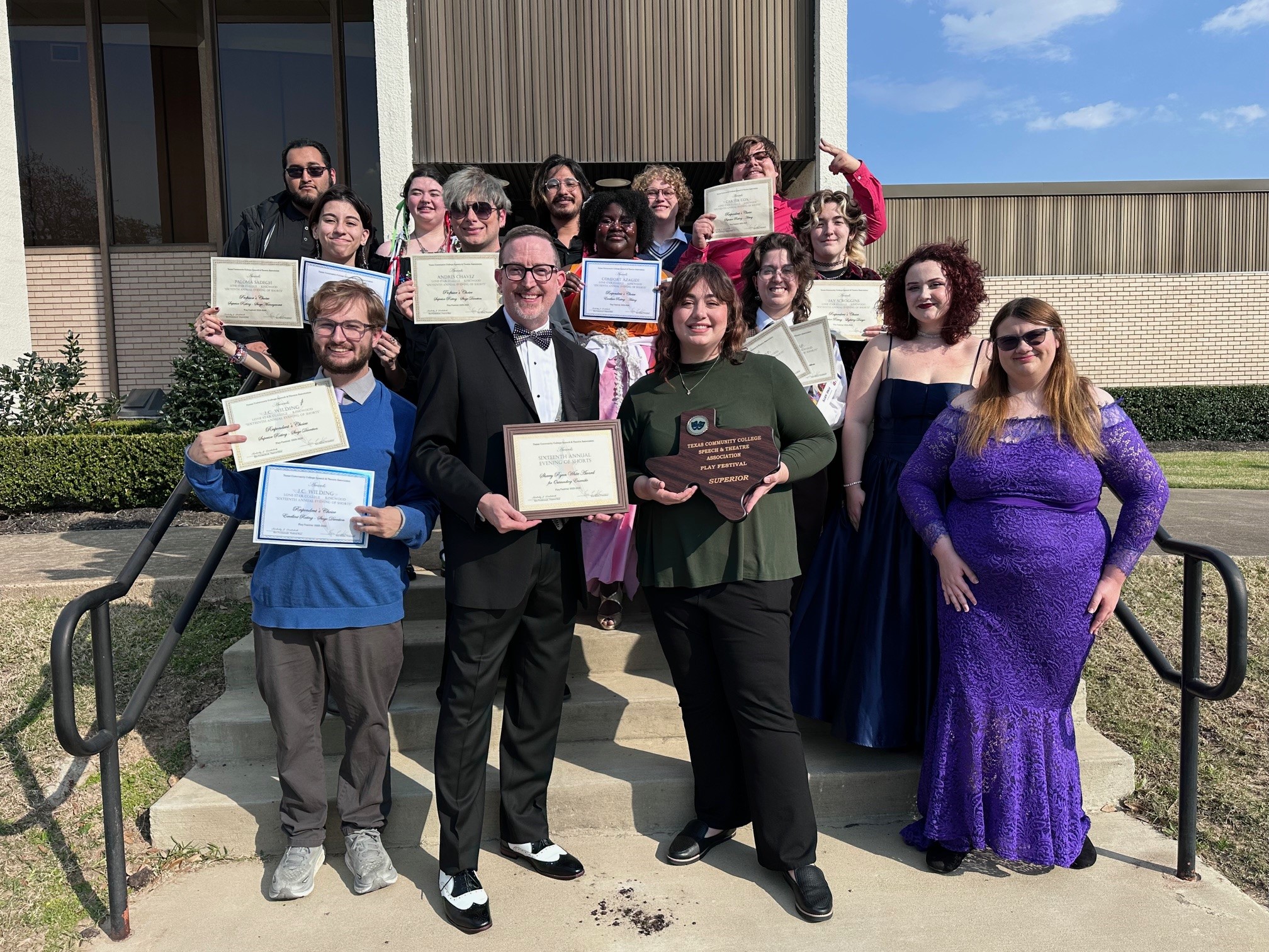 The LSC-K Theatre celebrates their achievements at the recent 2026 TCCSTA state play festival. A group of directors and students stand on stairs in fancy dress holding up awards and certificates while smiling at the camera.
