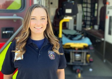 Emergency Medical Services student with open ambulance and stretcher behind her