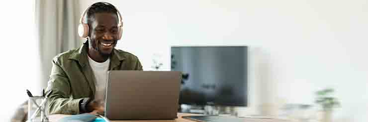 Man wearing headphones smiling at a laptop while doing work.