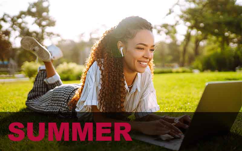 Woman laying in the grass smiling at her laptop.