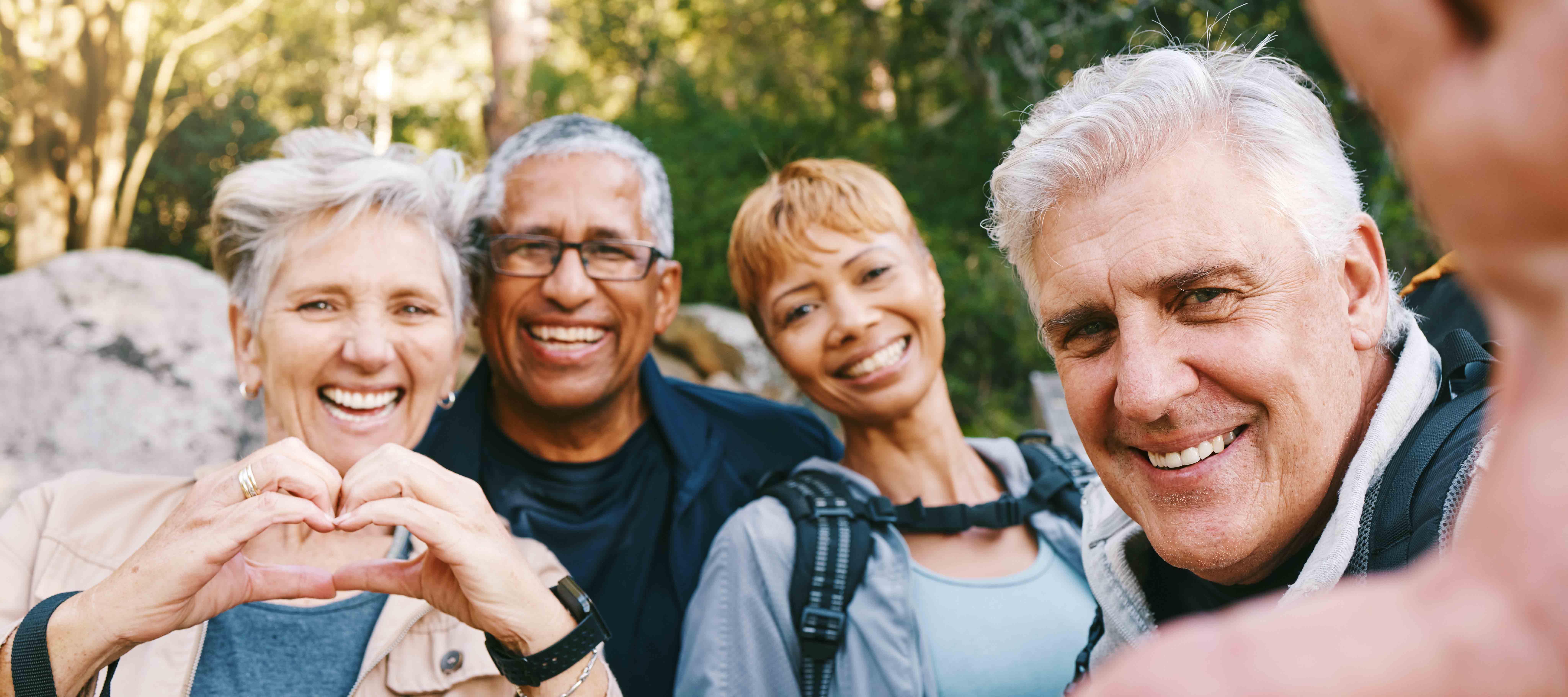 Image of four adults, two women and two men, taking a selfie while one woman holds her hands in a heart shape.