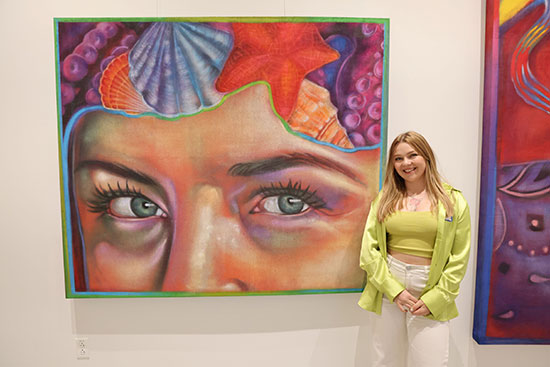 Lone Star College-University Park alum Taylor Barnes stands beside one of her large art murals from the Taylord: Anemoia exhibit.