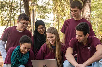 6 students outdoors surrounding a laptop